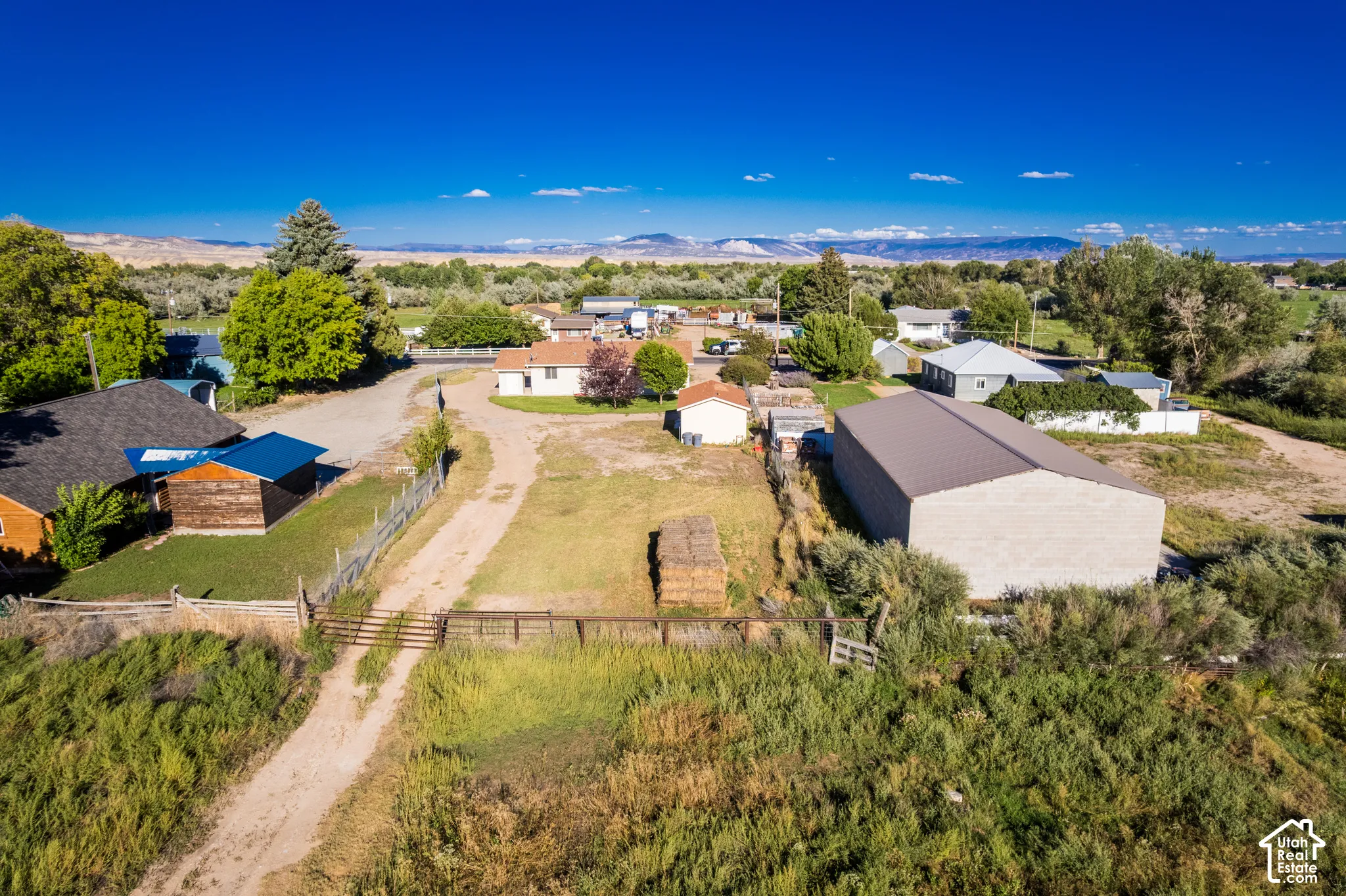 Expansive rural setting featuring a large metal-sided outbuilding, a fenced perimeter, and a dirt road entrance