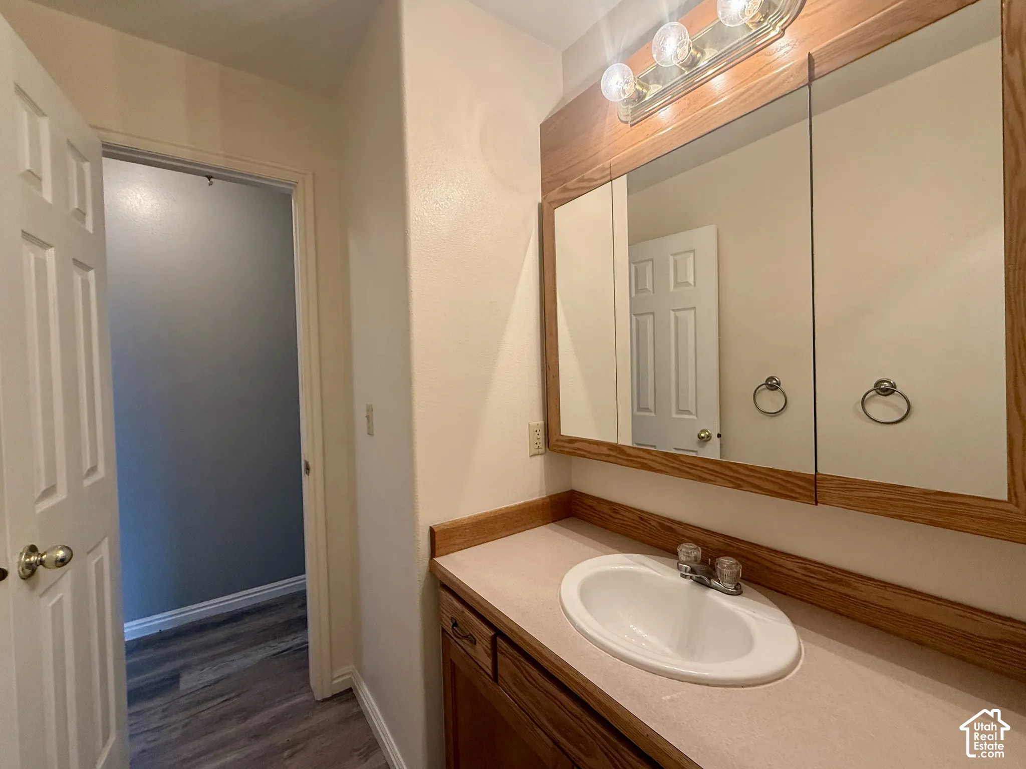 White oval sink with chrome faucet, wood-finish vanity with drawer, and a matching wood-finish medicine cabinet with integrated lighting