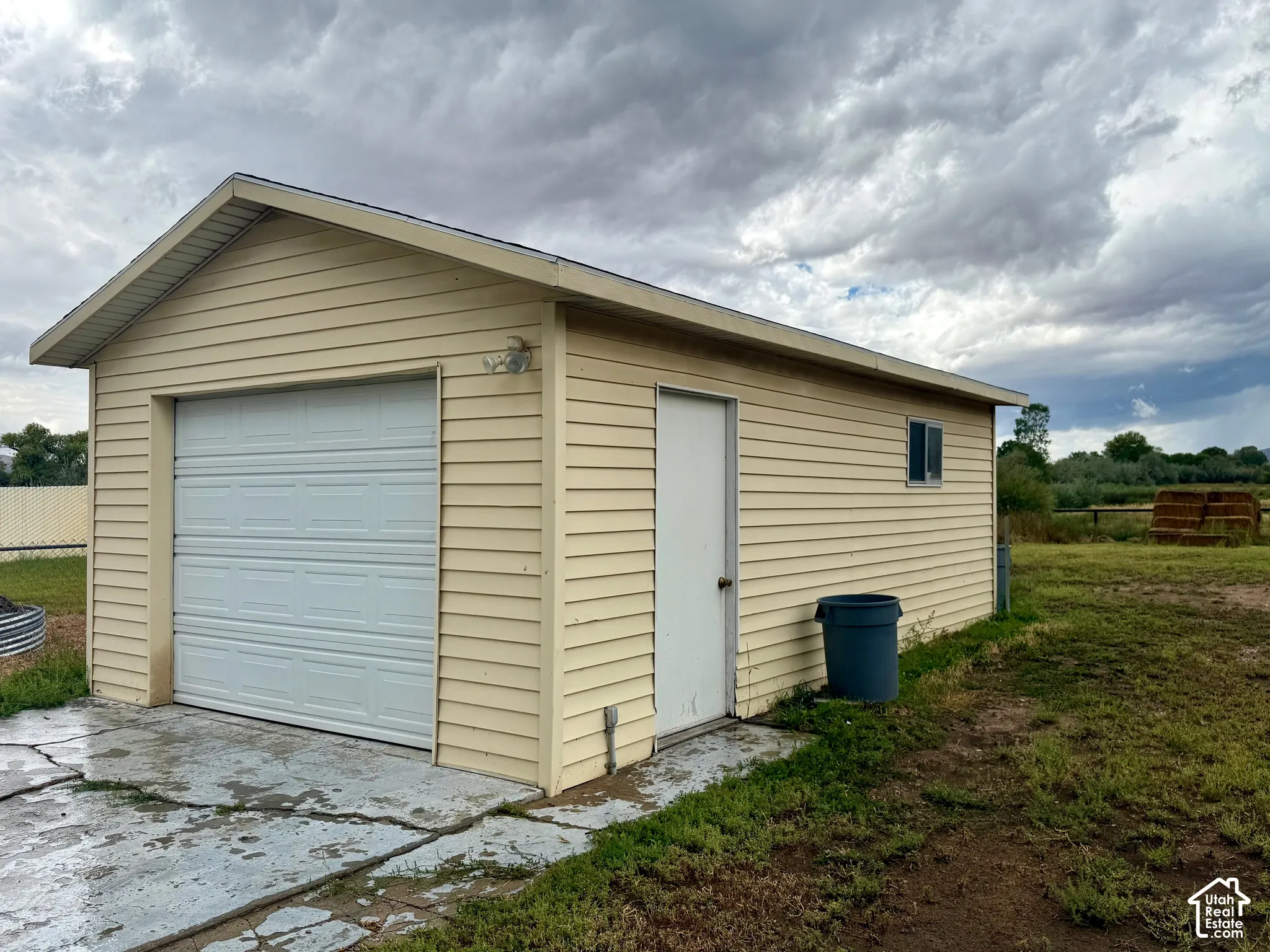 Detached outbuilding with light-colored siding, a single garage door, a side entry door, and a window