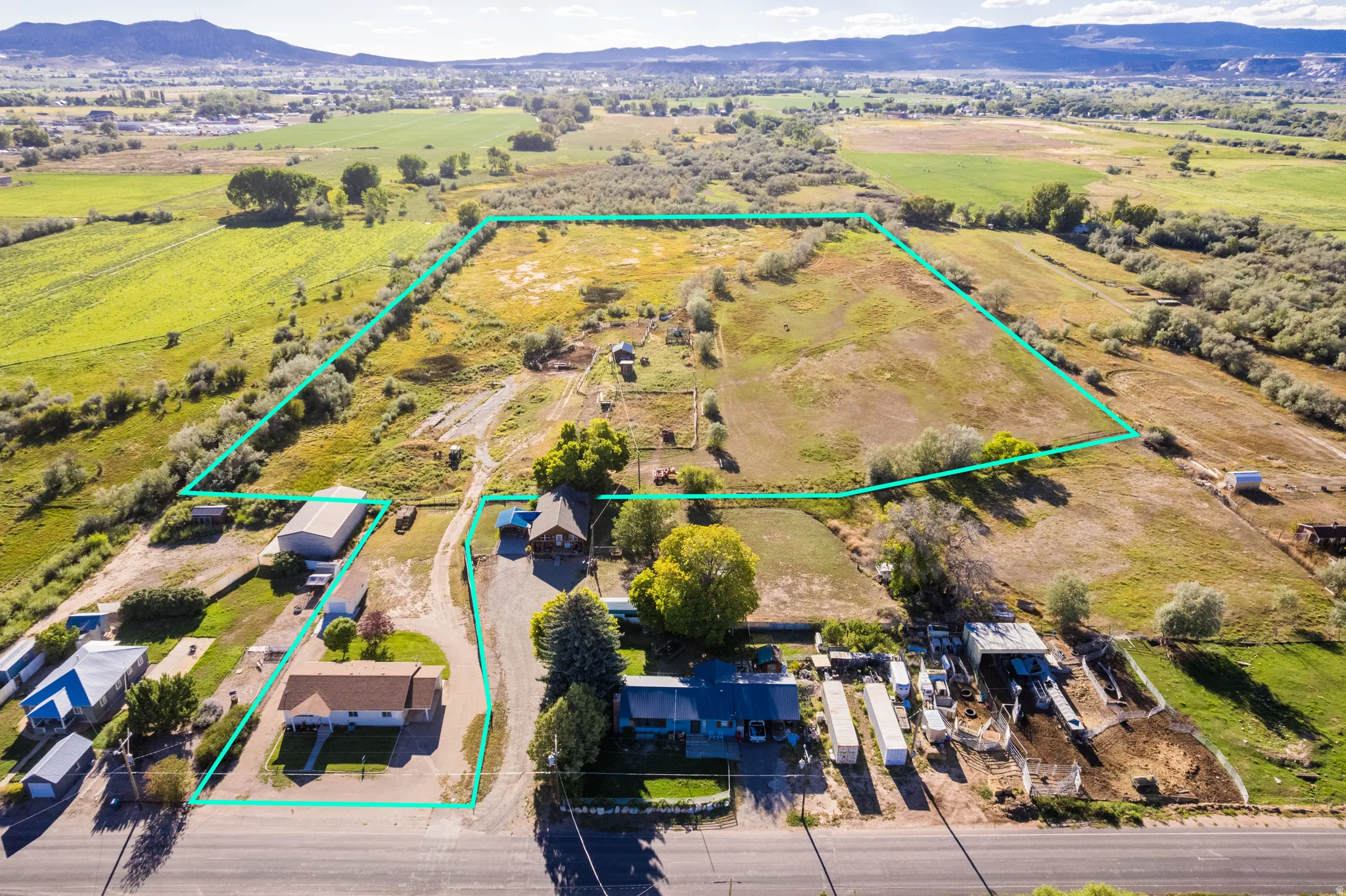 Expansive property featuring multiple structures, open land, paved road frontage, and a mountain backdrop