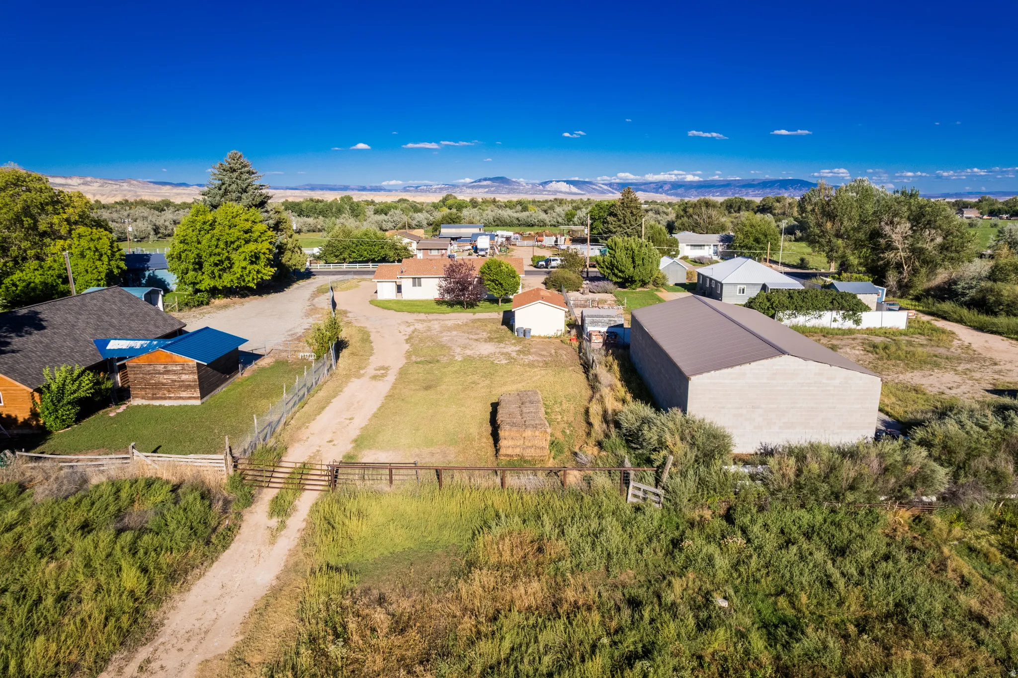 Expansive rural setting featuring a large metal-sided outbuilding, a fenced perimeter, and a dirt road entrance