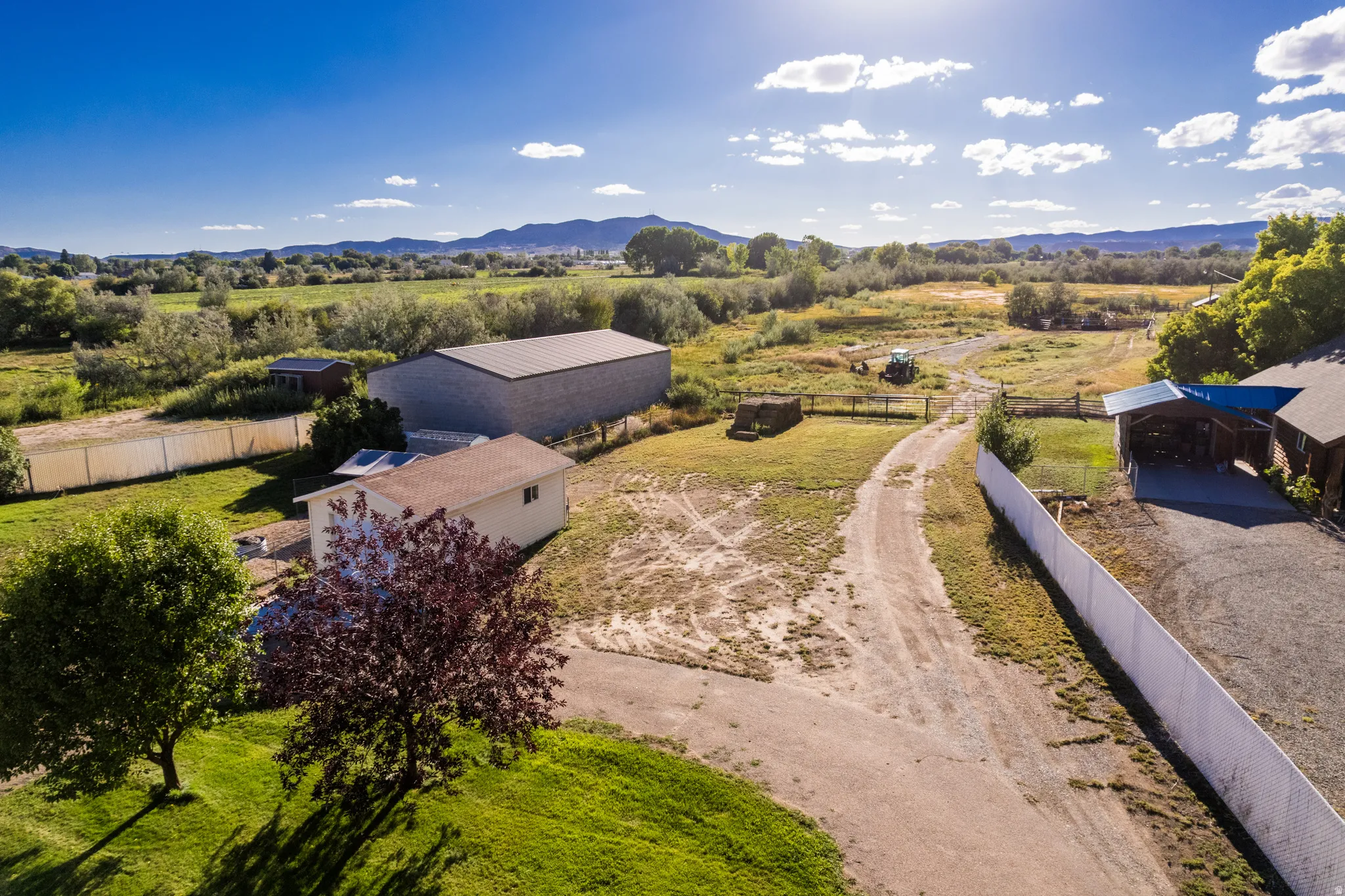 Expansive rural property featuring multiple structures, a gravel driveway, a large metal-roofed outbuilding, and a white privacy fence