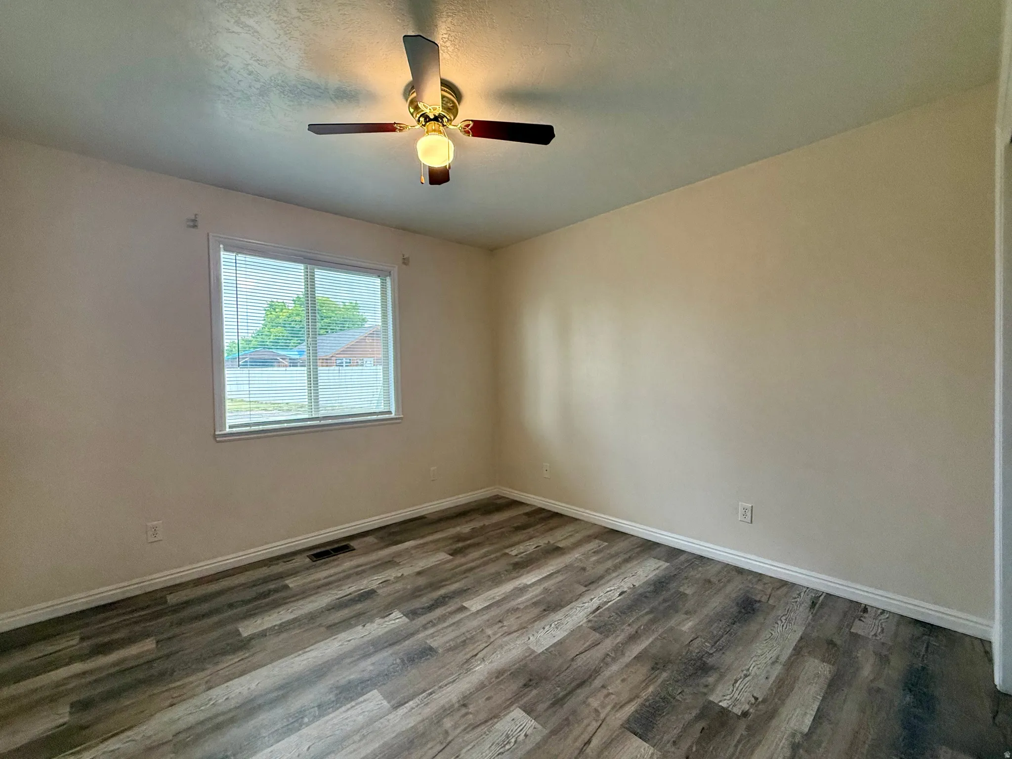 Wood-finish flooring, neutral wall tones, ceiling fan with integrated lighting, and a window with blinds