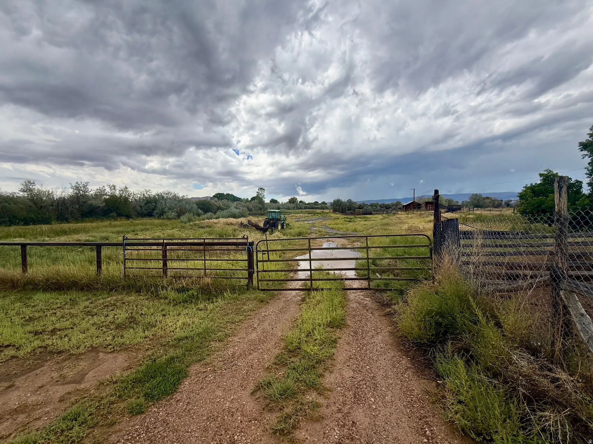 Gravel driveway entry with a metal gate, leading to an expansive undeveloped parcel featuring natural vegetation and distant structures