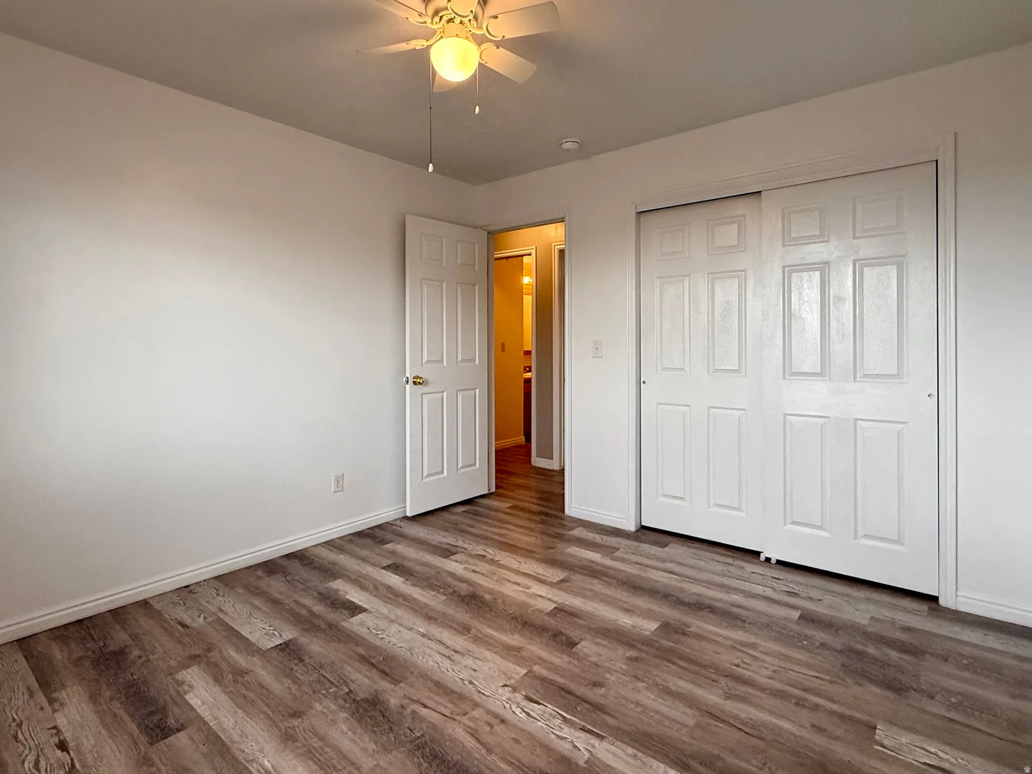 Wood-finish flooring, ceiling fan, white paneled doors, and a bi-fold closet