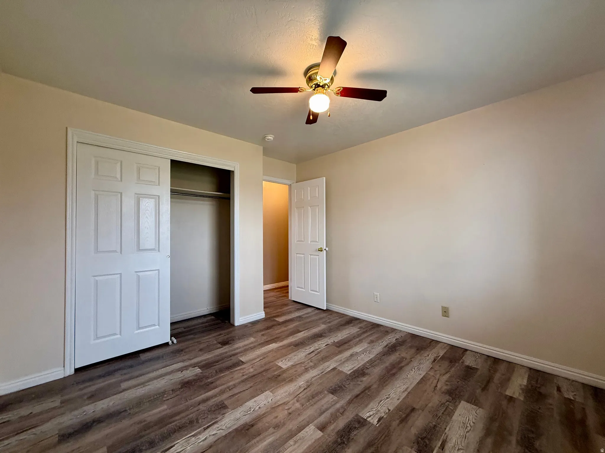 Wood-finish flooring, ceiling fan with light fixture, neutral wall palette, bi-fold closet doors, and interior paneled door