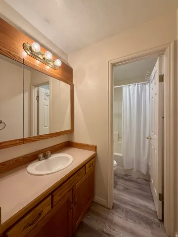 Bathroom featuring a wood-finish vanity with an integrated sink, laminate countertop, and a medicine cabinet with an overhead light fixture