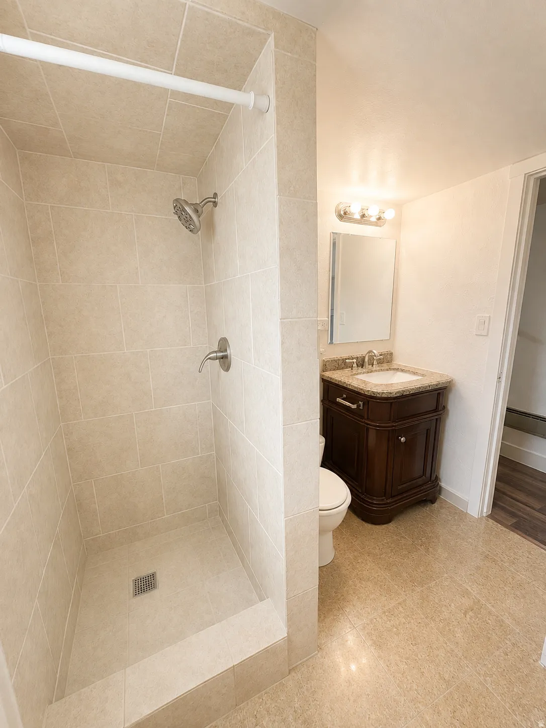 Tiled shower enclosure with a rainfall showerhead, and a vanity with an undermount sink and stone countertop