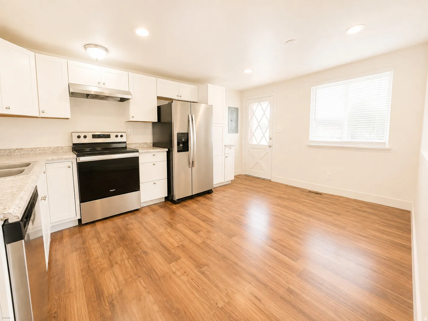 White cabinetry, stainless steel appliances, wood-finish flooring, recessed lighting, and a white paneled door