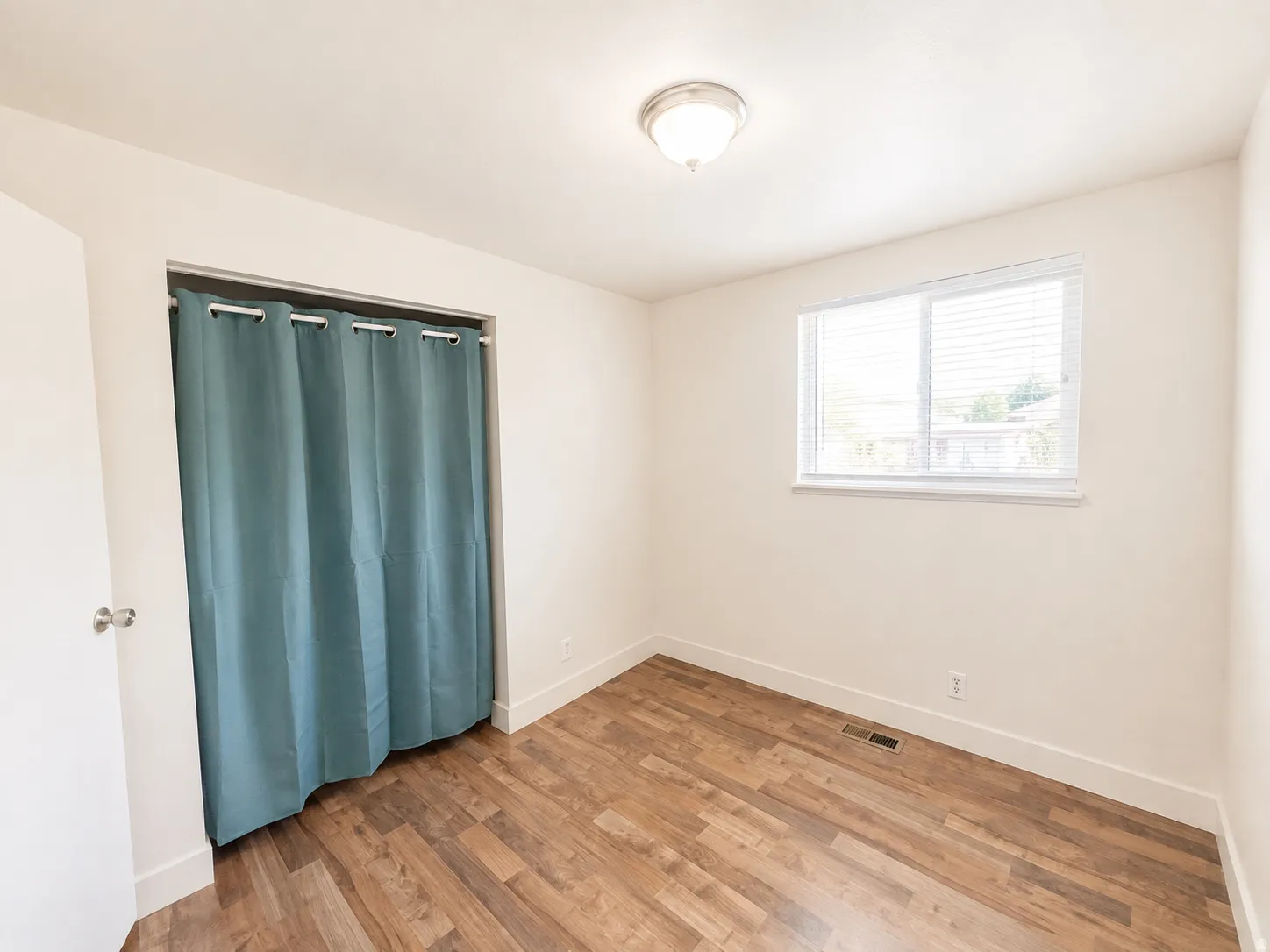 Wood-finish flooring, white walls, and a multi-pane window with horizontal blinds