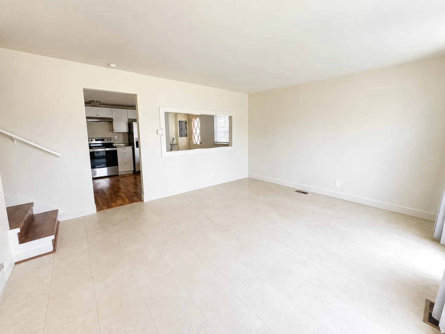 Spacious room with light-colored tile flooring, white walls, and a pass-through window to the kitchen
