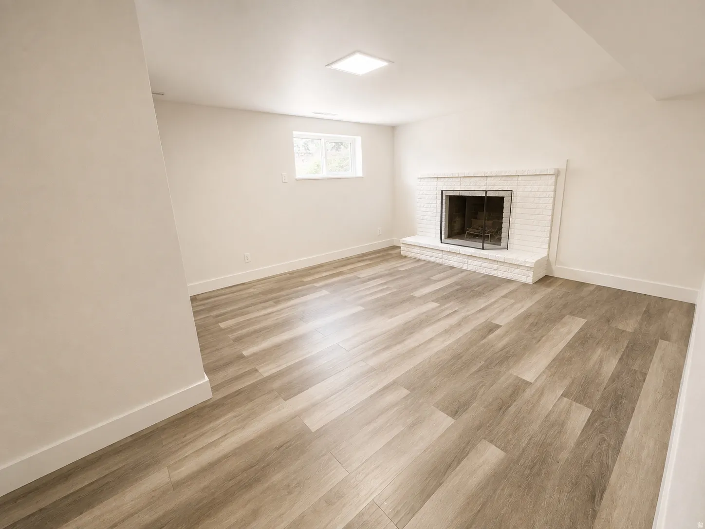 Wood-finish flooring, white brick fireplace, white walls, flush-mount ceiling light, and a window