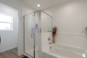 Enclosed shower with clear glass door, built-in bathtub, recessed ceiling lighting, and wood-finish flooring