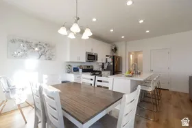 White cabinetry, recessed lighting, stainless steel appliances, kitchen island with counter seating, and wood-finish flooring