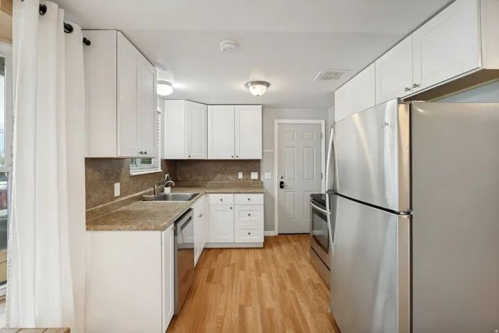 White cabinetry with dark hardware, stainless steel appliances, wood-finish flooring, and a window over the sink