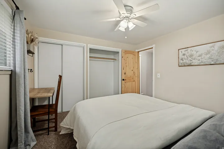 Recessed window with blinds, ceiling fan with integrated lighting, wood-finish door with black hardware, and built-in closet with sliding doors