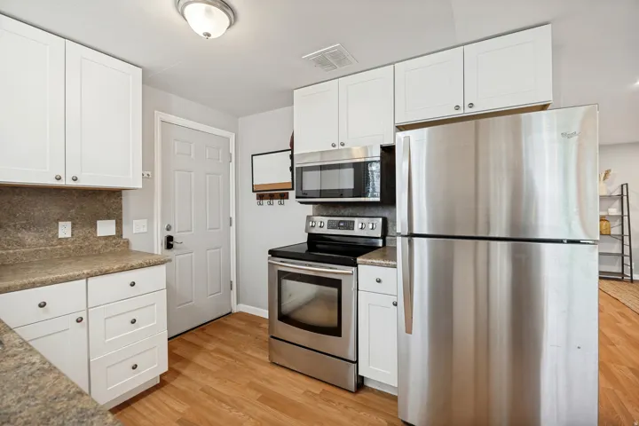 Kitchen featuring stainless steel appliances, white cabinetry, wood-finish flooring, and a built-in microwave