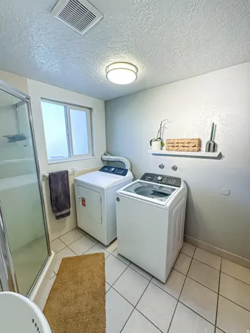 Functional utility space featuring a shower enclosure, window, tiled flooring, and a wall-mounted shelf