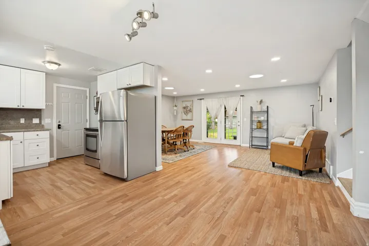 Open-concept living area with wood-finish flooring, white cabinetry, stainless steel appliances, and double doors opening to the exterior