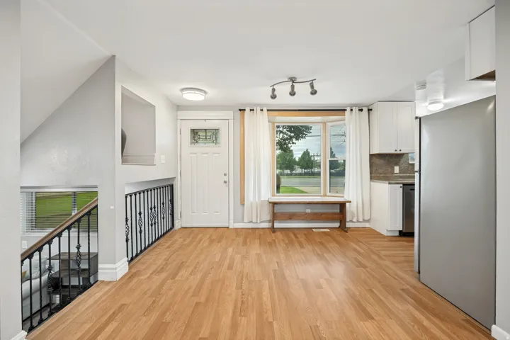 Wood-finish flooring throughout, white kitchen cabinetry, stainless steel appliances, bay window, and decorative iron stair railing