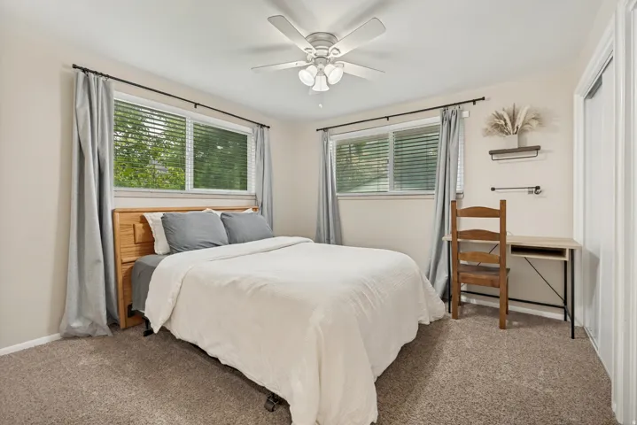 Neutral wall color, ceiling fan with integrated lighting, two windows with blinds, and carpeted flooring