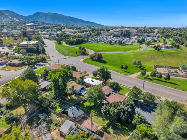 Expansive aerial perspective featuring surrounding green spaces, paved roads, and distant mountains