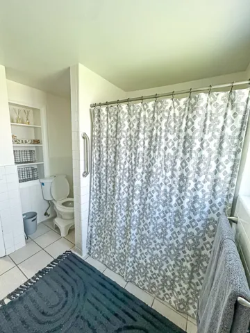 White tile flooring with built-in shelving, a shower grab bar, and a towel bar
