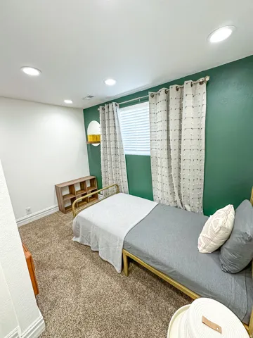 Recessed ceiling lighting, textured carpet flooring, window with blinds and curtains, and accent wall