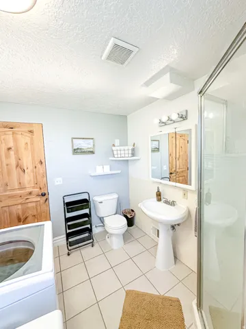 Pedestal sink with a wall-mounted mirror, ceramic tile flooring, and a glass-enclosed shower