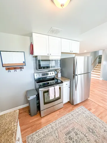 Stainless steel appliances, white cabinetry, wood-finish flooring, and granite-style countertops