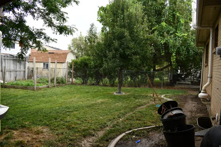 Expansive rear yard featuring mature trees, a chain-link fence, and a storage shed with a gambrel roof