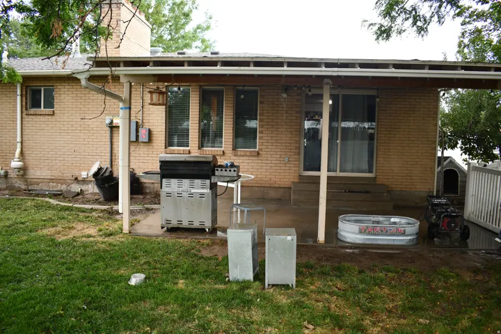 Brick exterior with a covered patio, concrete steps, sliding glass door, and a grass lawn