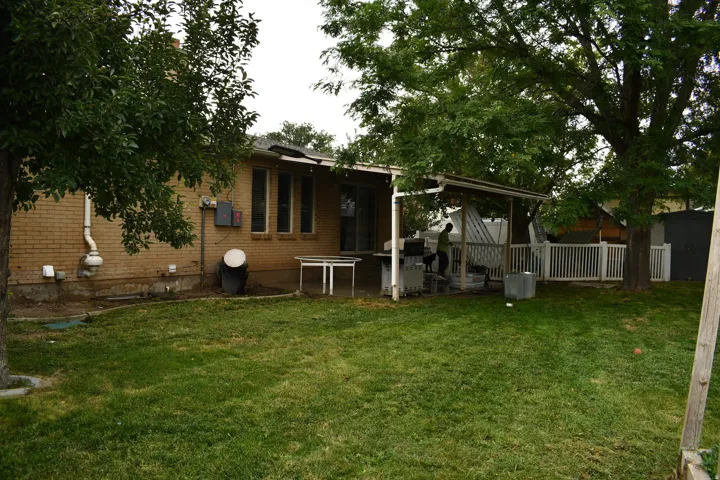 Expansive backyard featuring a brick exterior, mature trees, a covered patio structure, and a white picket fence