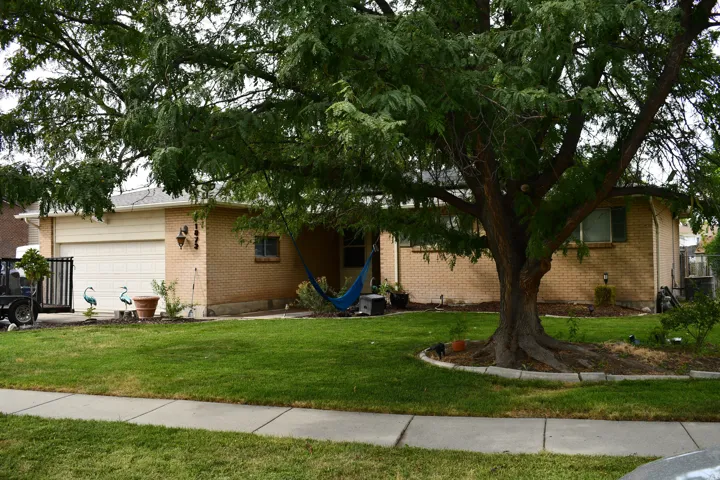Brick exterior with a large mature tree, attached garage, and manicured lawn