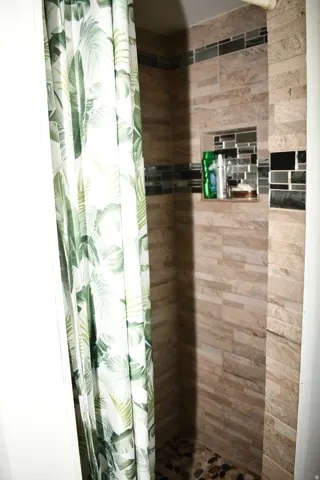 Tiled shower enclosure featuring a mosaic accent band, recessed niche with mosaic backing, and a river rock shower floor
