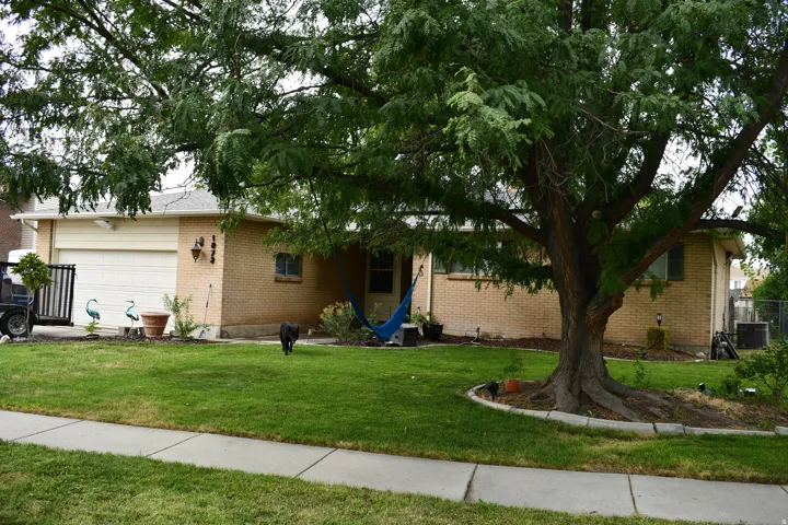 Brick exterior with a prominent mature tree, manicured lawn, and an attached garage with a white door