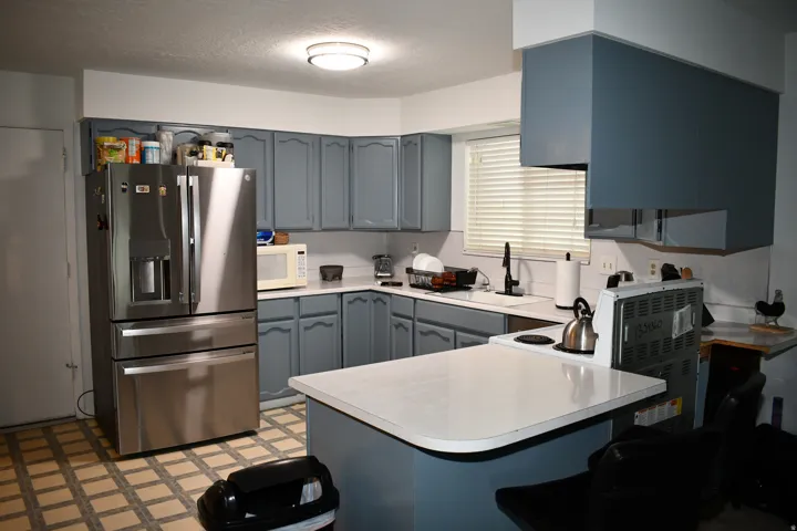 Stainless steel refrigerator, blue painted cabinetry, white countertops, and a black faucet