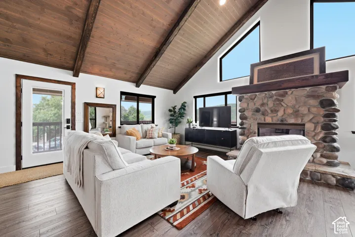Vaulted wood-paneled ceiling with exposed beams, stone-clad fireplace with wood mantel, multiple large windows, glass-paneled exterior door, and wood-finish flooring