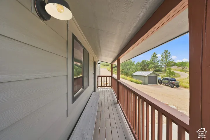 Covered porch with wood flooring and railing, light-colored siding, and exterior lighting fixture