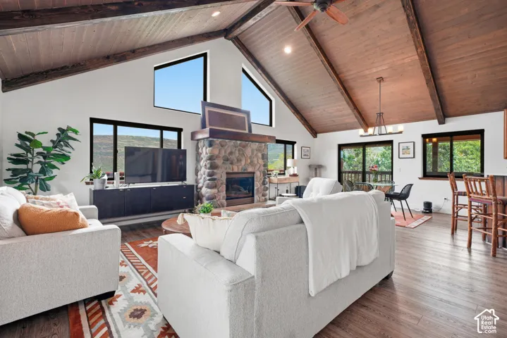 Vaulted wood-paneled ceiling with exposed beams, stone fireplace with a wood mantle, wood-finish flooring, and multiple windows