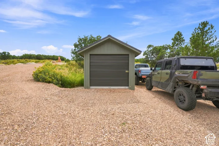 Freestanding outbuilding with a pitched roof and a roll-up garage door, set on a gravel surface