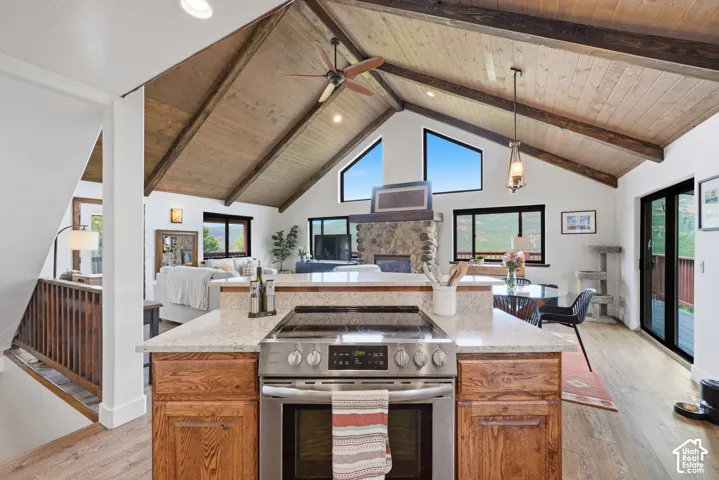 Vaulted wood-paneled ceilings with exposed beams, stone fireplace, stainless steel range, wood-finish flooring, and sliding glass door access to an outdoor area