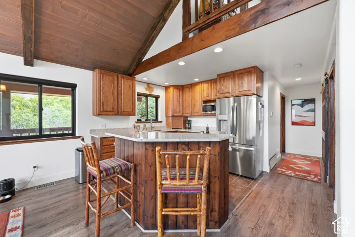 Warm wood cabinetry and beam detailing define this kitchen, featuring stainless steel appliances, wood-finish flooring, and a centered island with seating