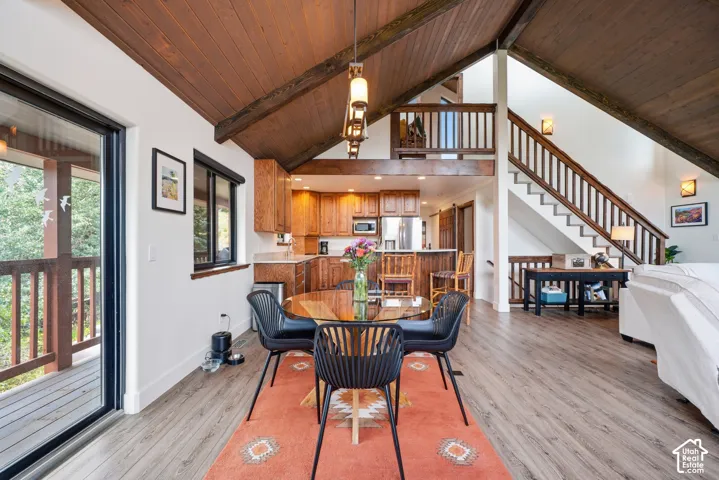Vaulted wood-paneled ceiling with exposed beams, wood-finish flooring, kitchen with wood cabinetry and stone-look countertops, sliding glass door access to an exterior deck, and a multi-level staircase with wood railings