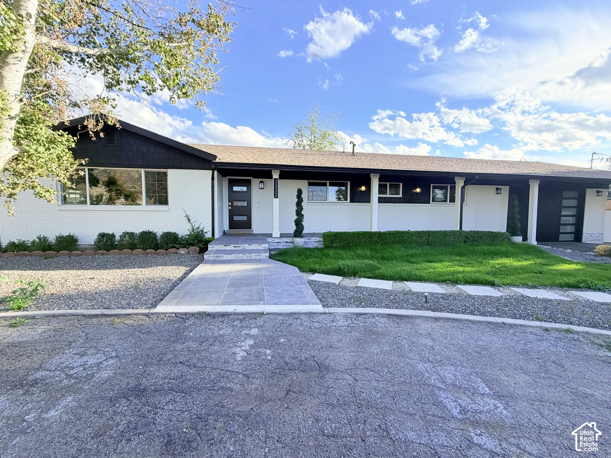 Contemporary exterior featuring a black modern entry door, white brick facade, dark trim, and a concrete paver walkway