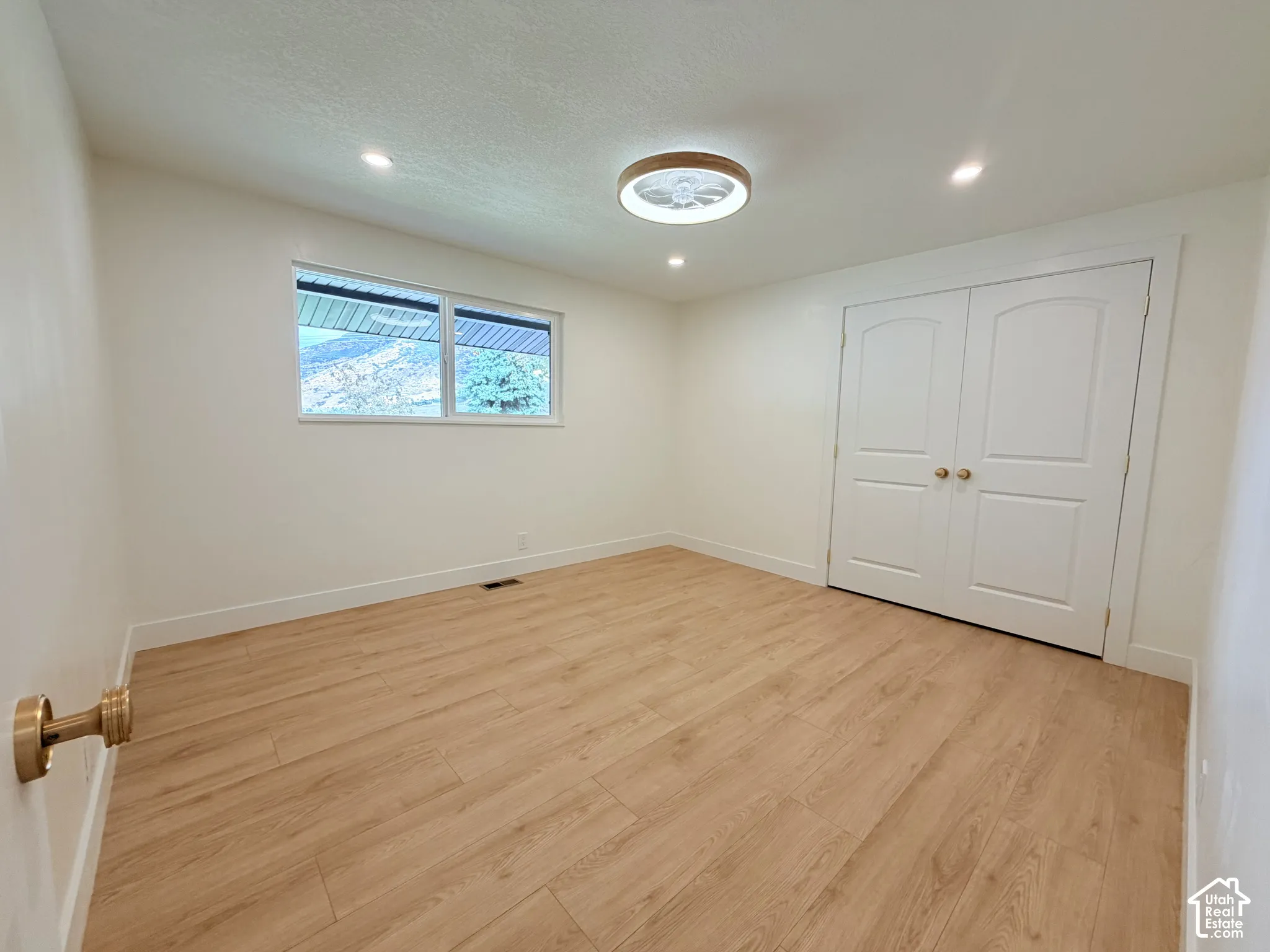 Wood-finish flooring, recessed lighting, ceiling light fixture, white interior walls, and bi-fold closet doors with brass hardware