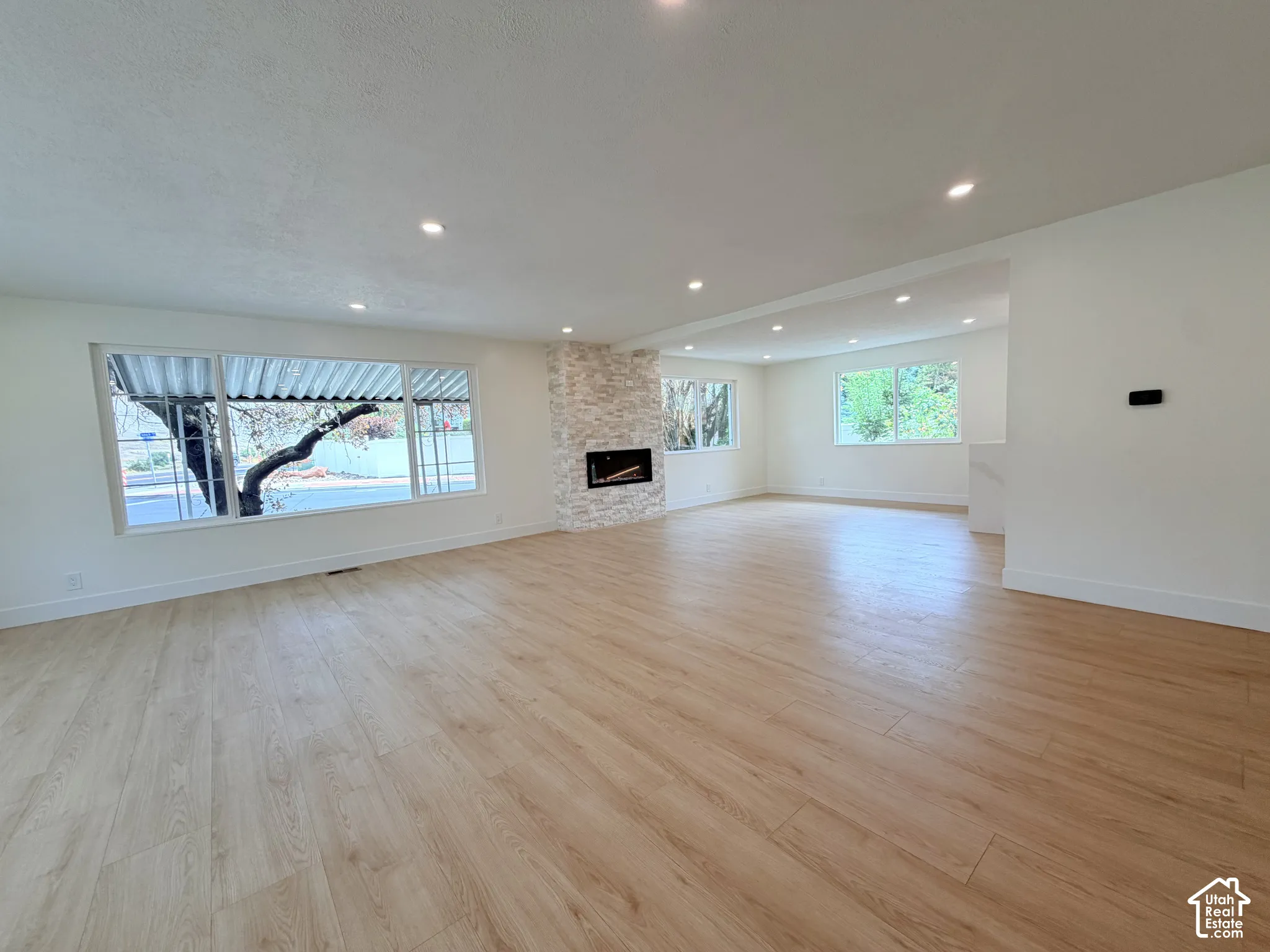 Expansive living area featuring wood-finish flooring, recessed lighting, multiple large windows, and a stone-clad fireplace