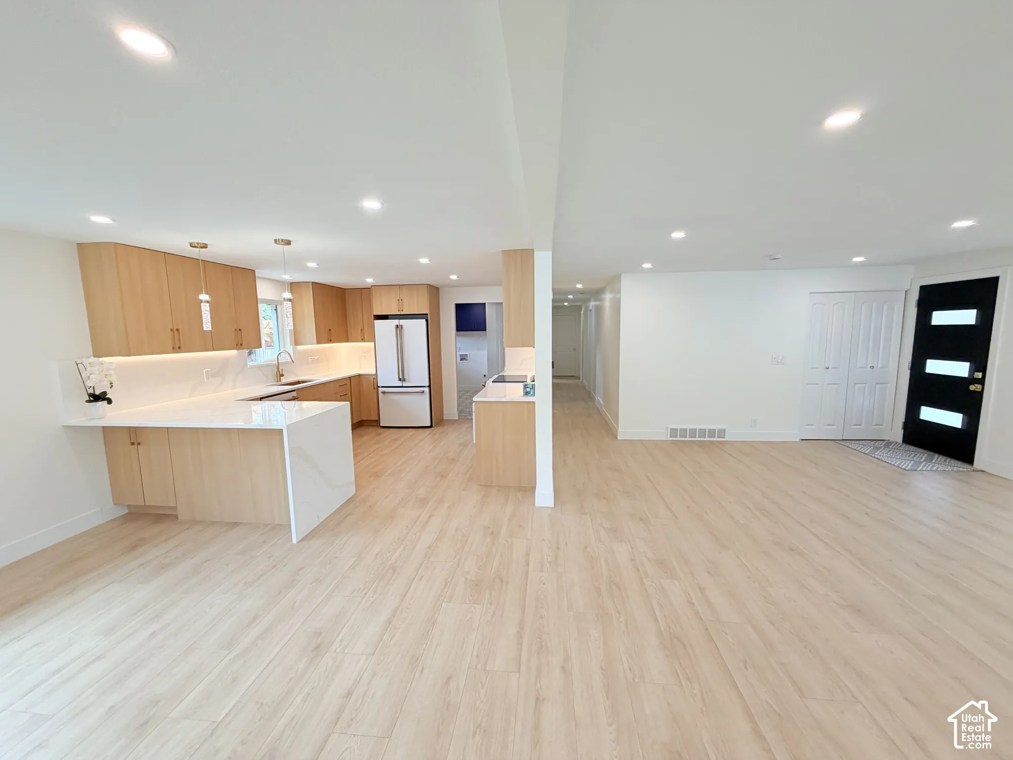 Open-concept living space with light wood-finish flooring, recessed lighting, a kitchen island with a waterfall countertop, and light wood cabinetry