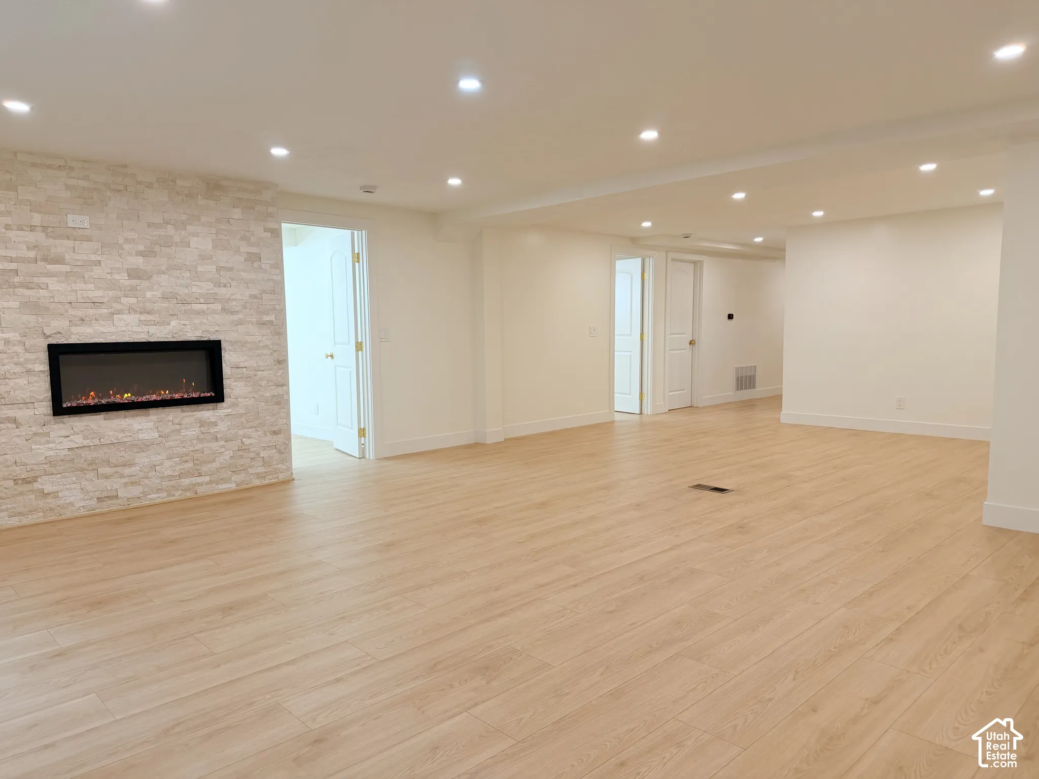 Expansive open-concept room featuring wood-finish flooring, recessed lighting, and a stone-clad wall with an integrated electric fireplace