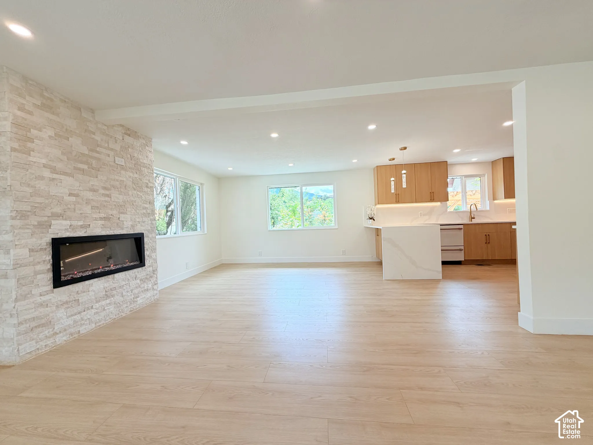 Recessed lighting, wood-finish flooring, stone-clad fireplace, kitchen island with waterfall countertop, and wood cabinetry